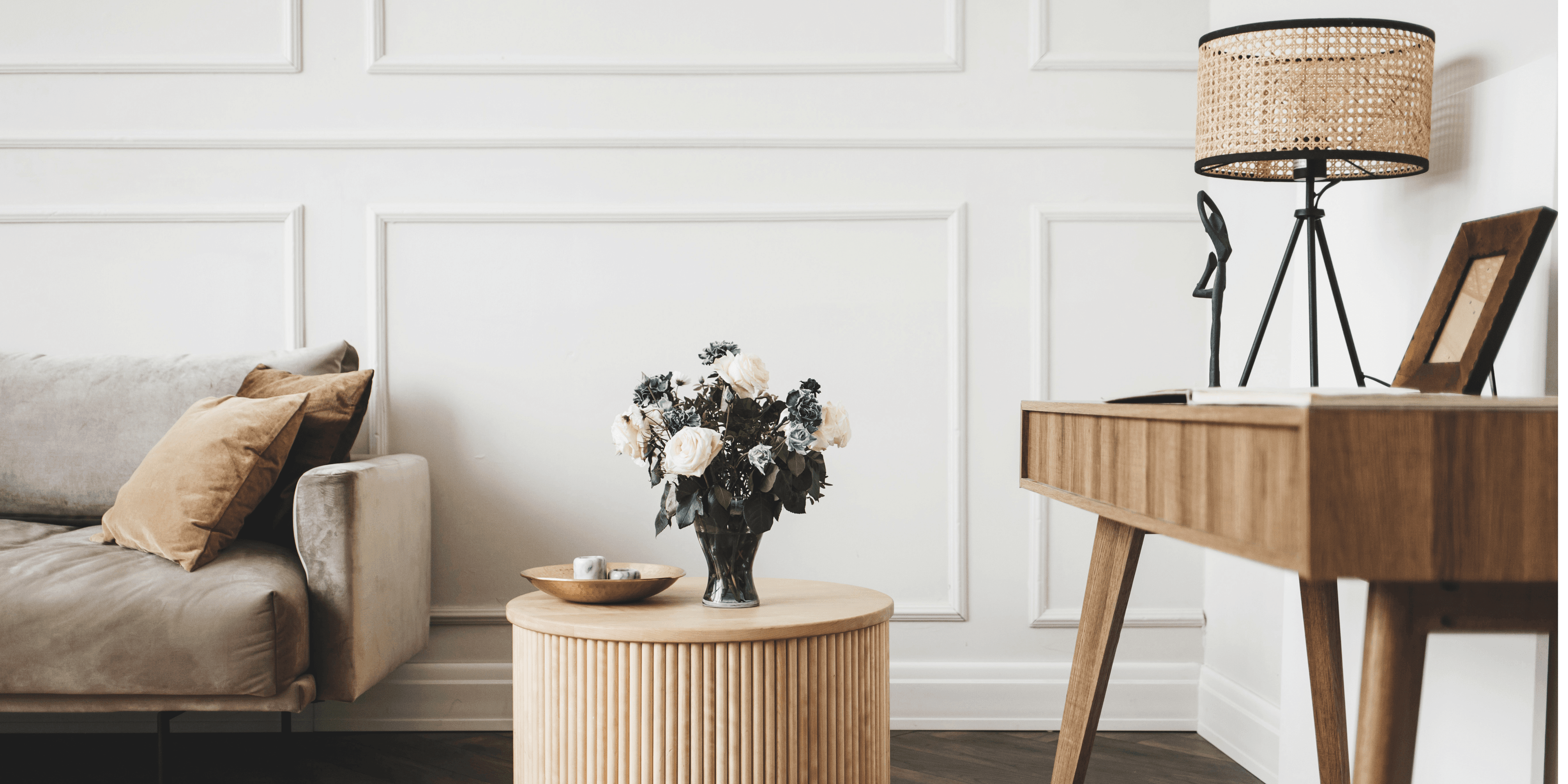 Olohuoneen nurkkaus, jossa on sohva, puinen sohvapöytä sekä sivupöytä. Huone on vaalea ja sisustuksessa on käytetty erisävyisiä puisia elementtejä. Sohvapöydällä on kukkakimppu.