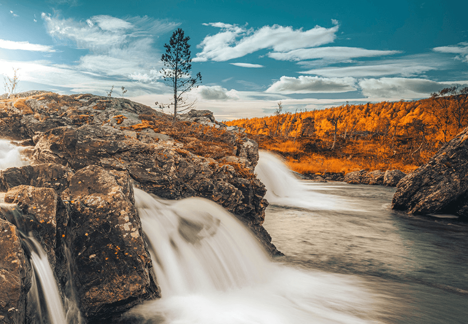 Syksyinen luontokuva, jossa vesivoima vyöryy vauhdilla kalliolta alas. 