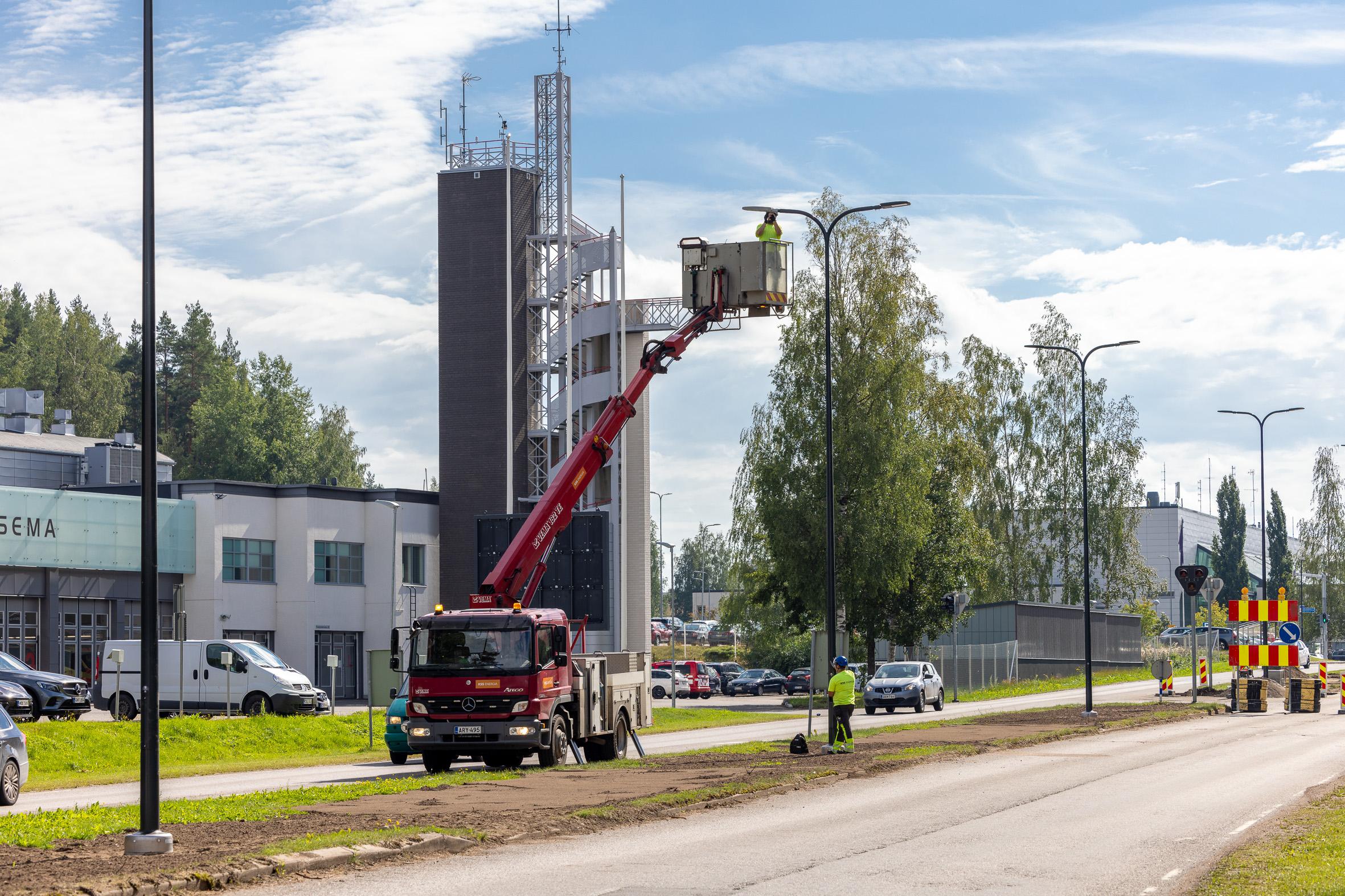 Punaisen kuorma-auton nostokorilla nostettu henkilö ilmaan asentamaan katuvaloa pylvääseen.