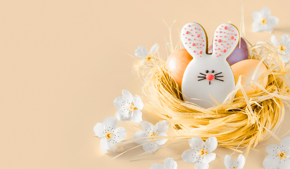Pääsiäisaiheinen kuva, jossa on oikeassa laidassa heinäpesässä piparista tehty pupu sekä pääsiäismunia. Pesän ympärille on ripoteltu pieniä valkoisia kukkia.