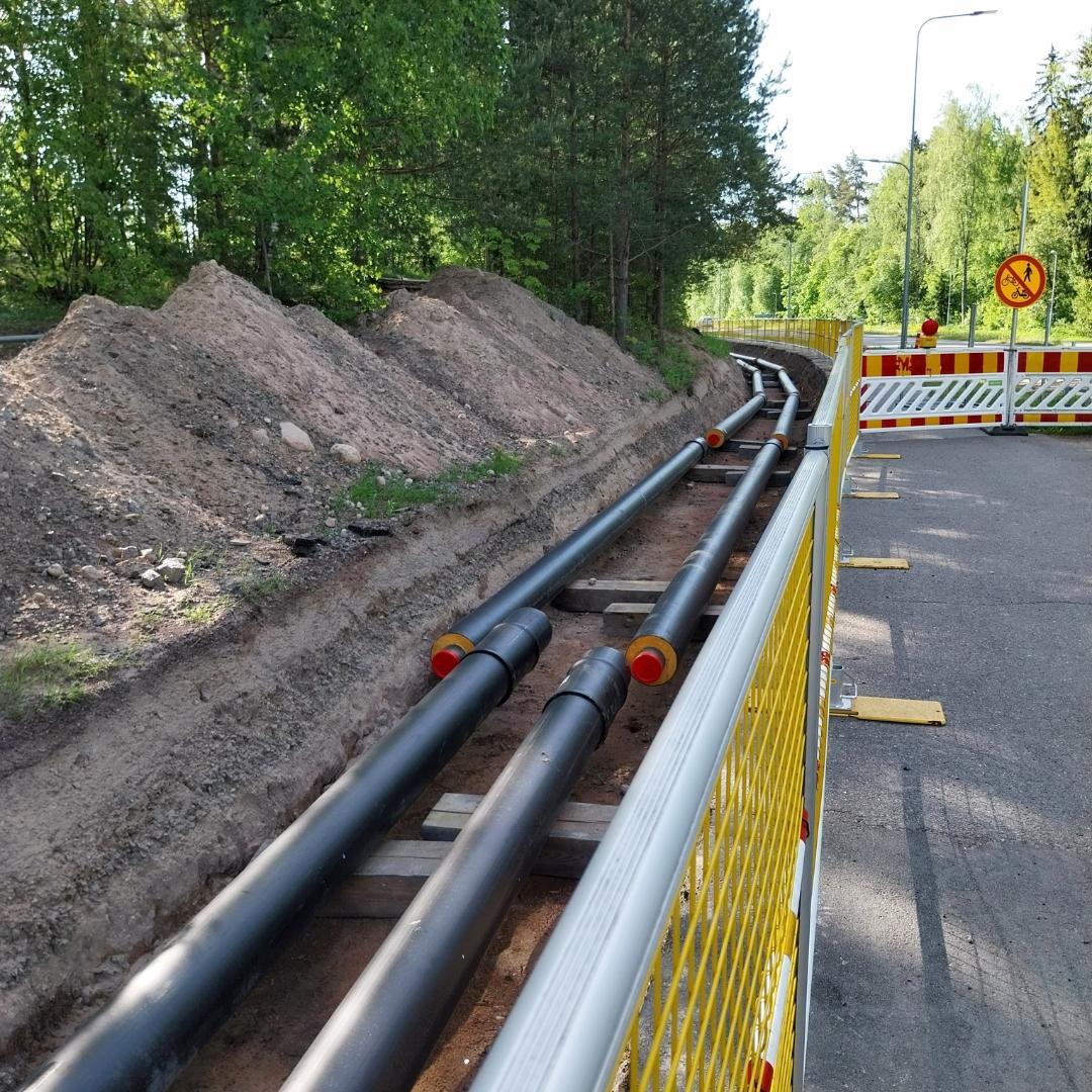 Kevyenliikenteenväylän reunasta on aidattu alue, johon on tehty kaivanto, jonka pohjalla näkyy vierekkäin kaksi mustaa paksua putkea.
