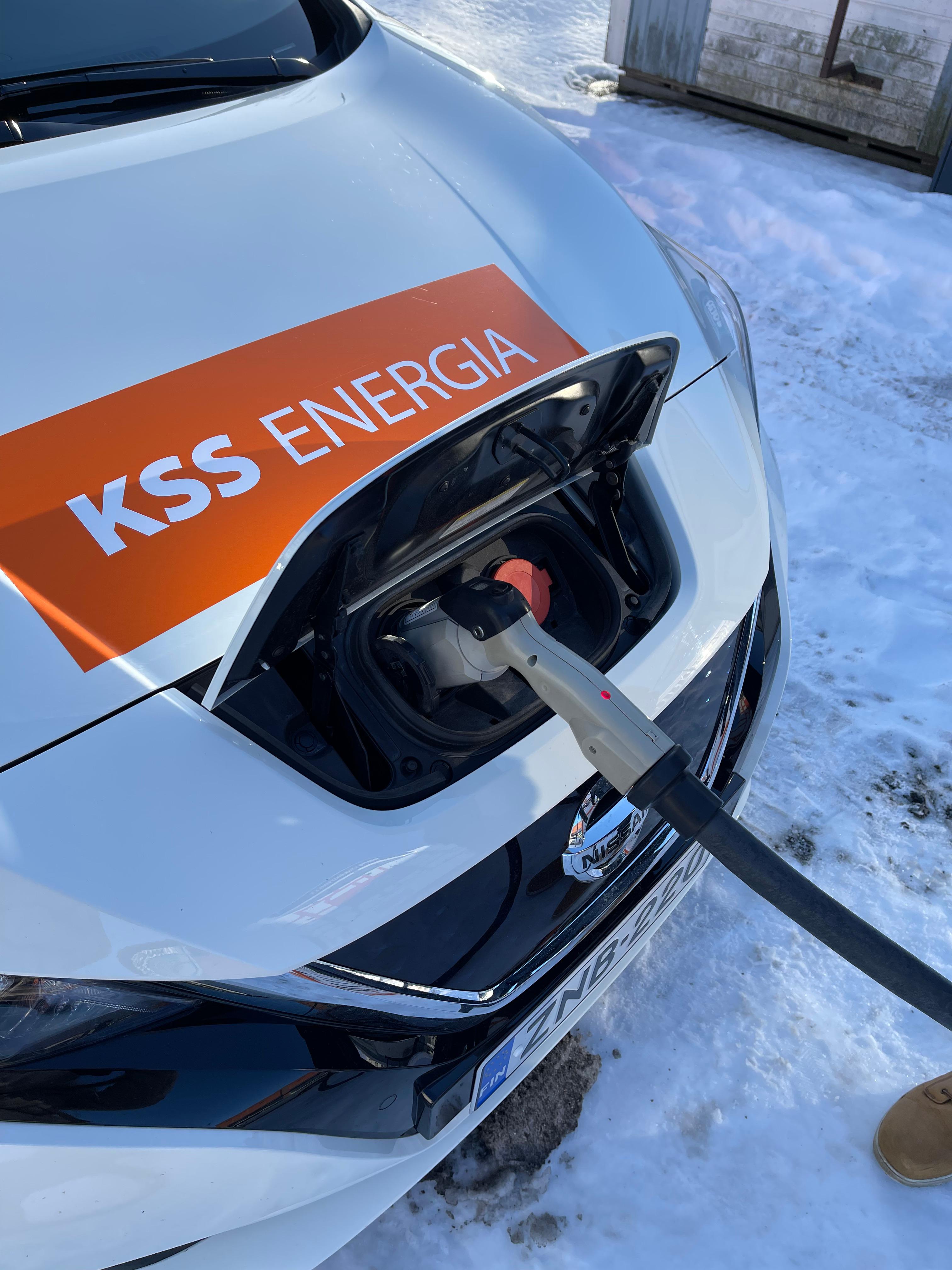 Valkoinen auto, jonka etuosassa on KSS Energian logo on latauksessa sähköauton latauspisteellä. Taustalla on lunta.