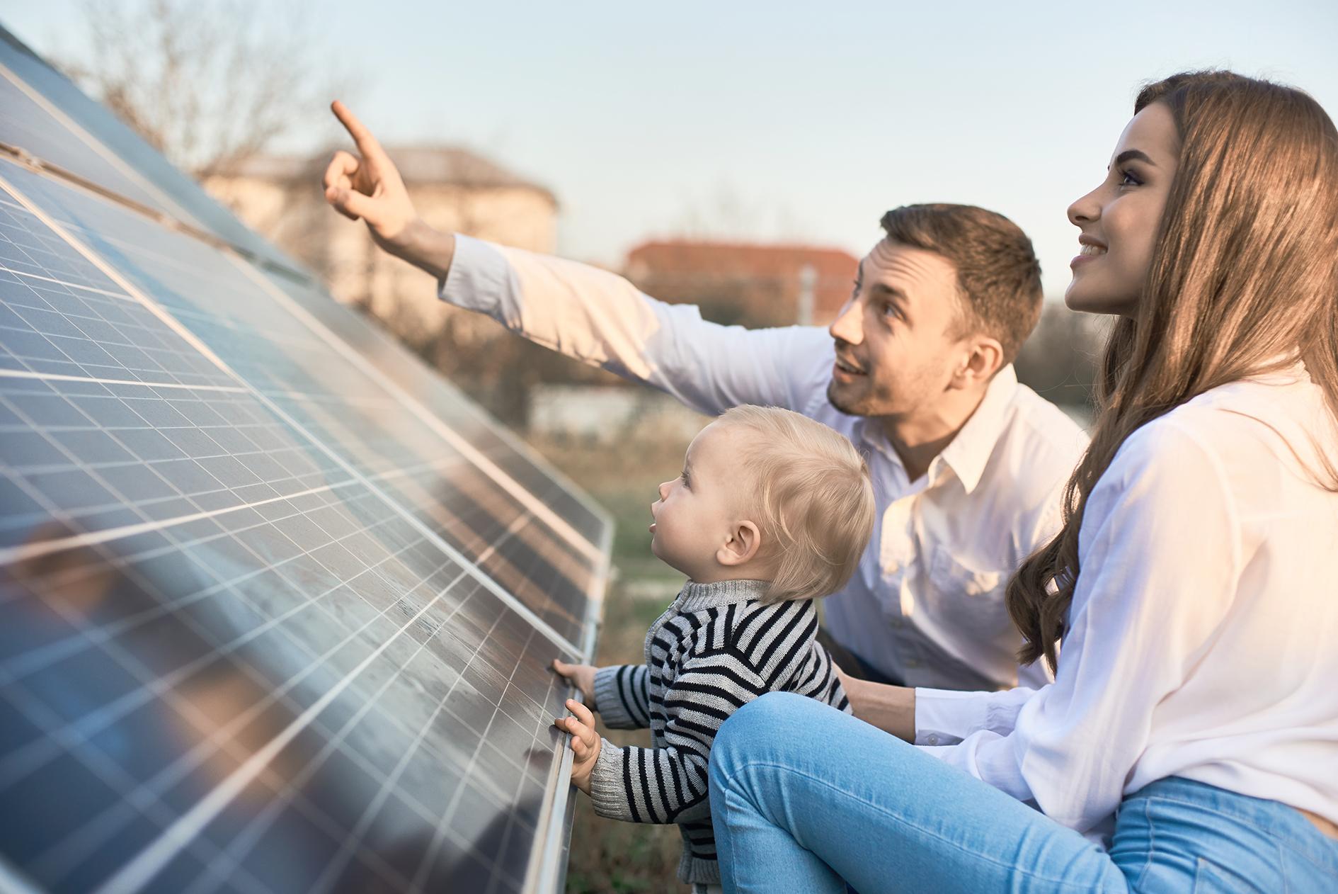 Isä, äiti ja pieni lapsi tutkivat maahan asennettuja aurinkopaneeleita.