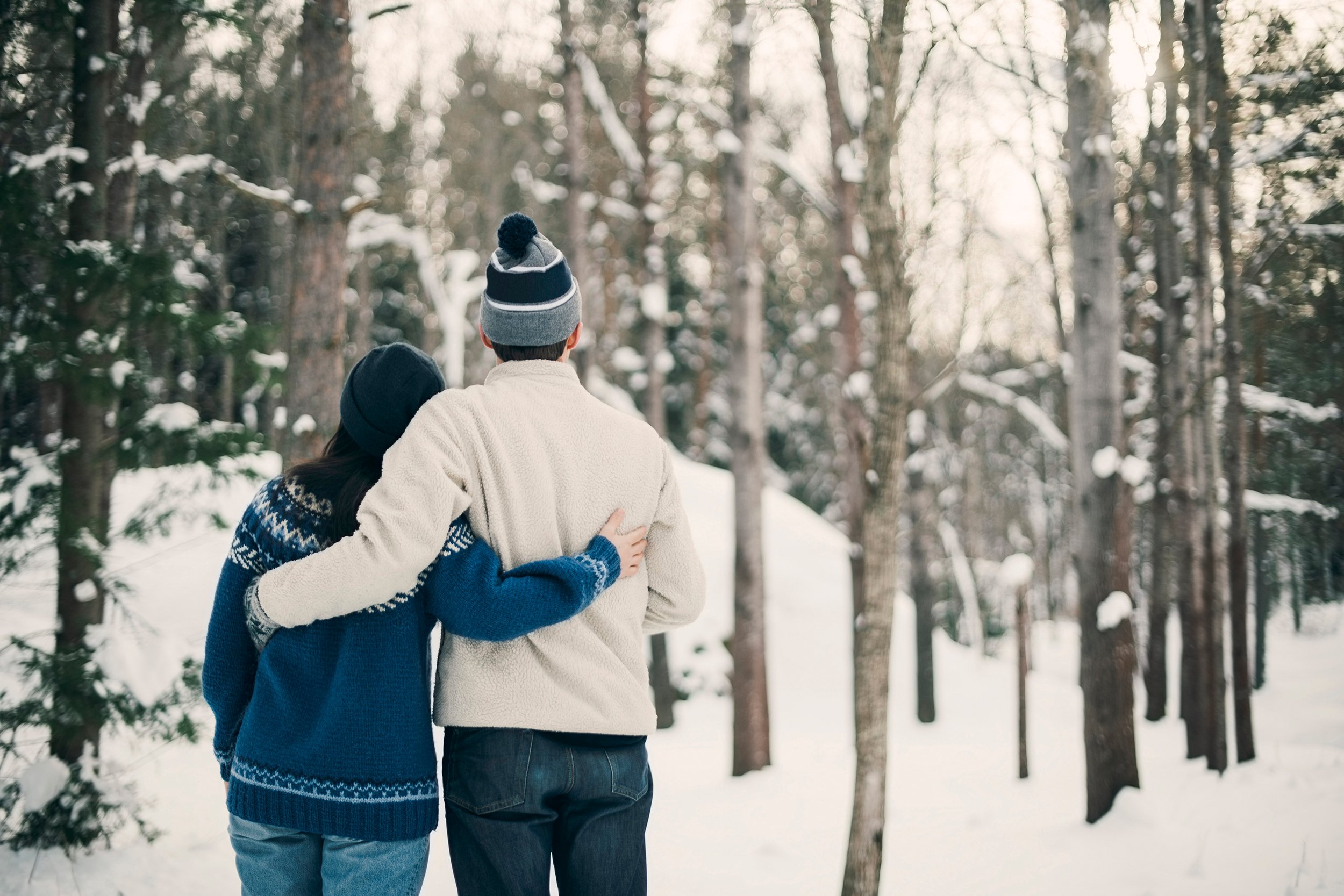Kuvassa näkyy pariskunta halaamassa talvisessa metsässä.