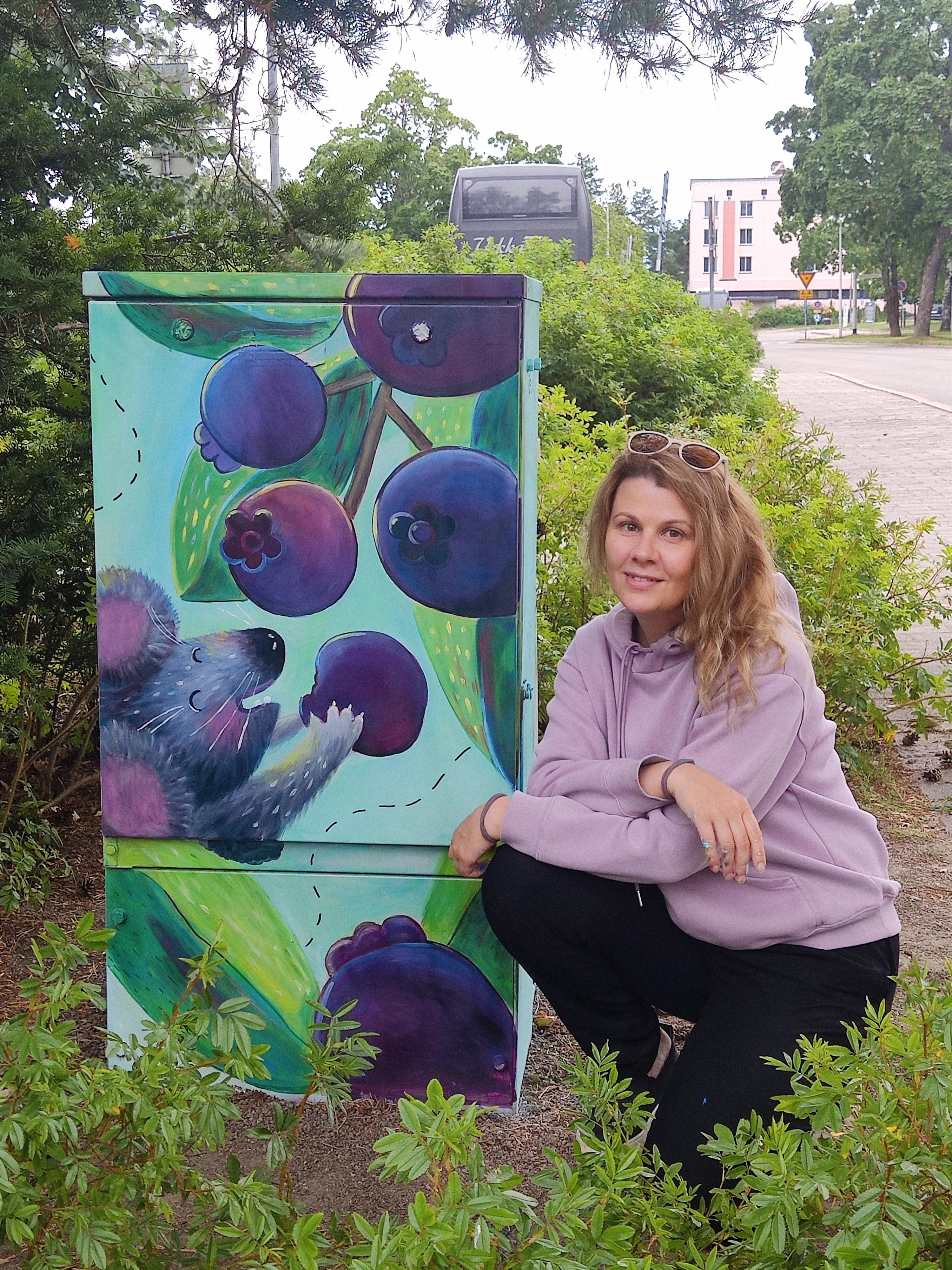 Kuvittaja Daria Savolainen poseeraa sähkönjakokaappiin tekemänsä hiiritaideteoksen vieressä.