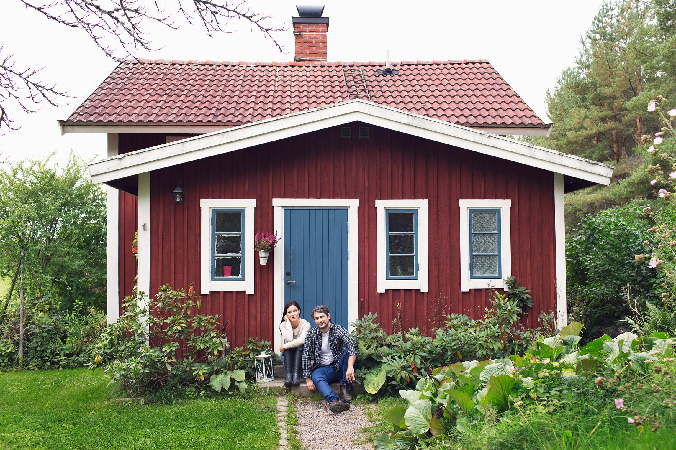 Mies ja nainen istuvat vierekkäin pienen punaisen mökin portaalla.