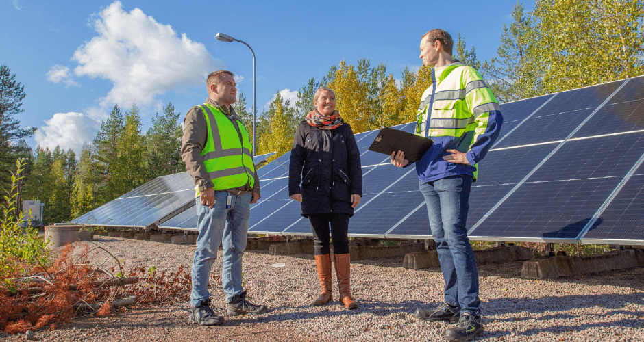 LSK Technologyn Marko Kyllästinen, Kymenlaakson Veden laitospäällikkö Emmi-Maria Ukko sekä KSS Energian tuotepäällikkö Mikko Suhonen keskustelemassa maa-asennettujen aurinkopaneelien edustalla. Taustalla vihreää metsää ja sininen taivas poutapilvillä.