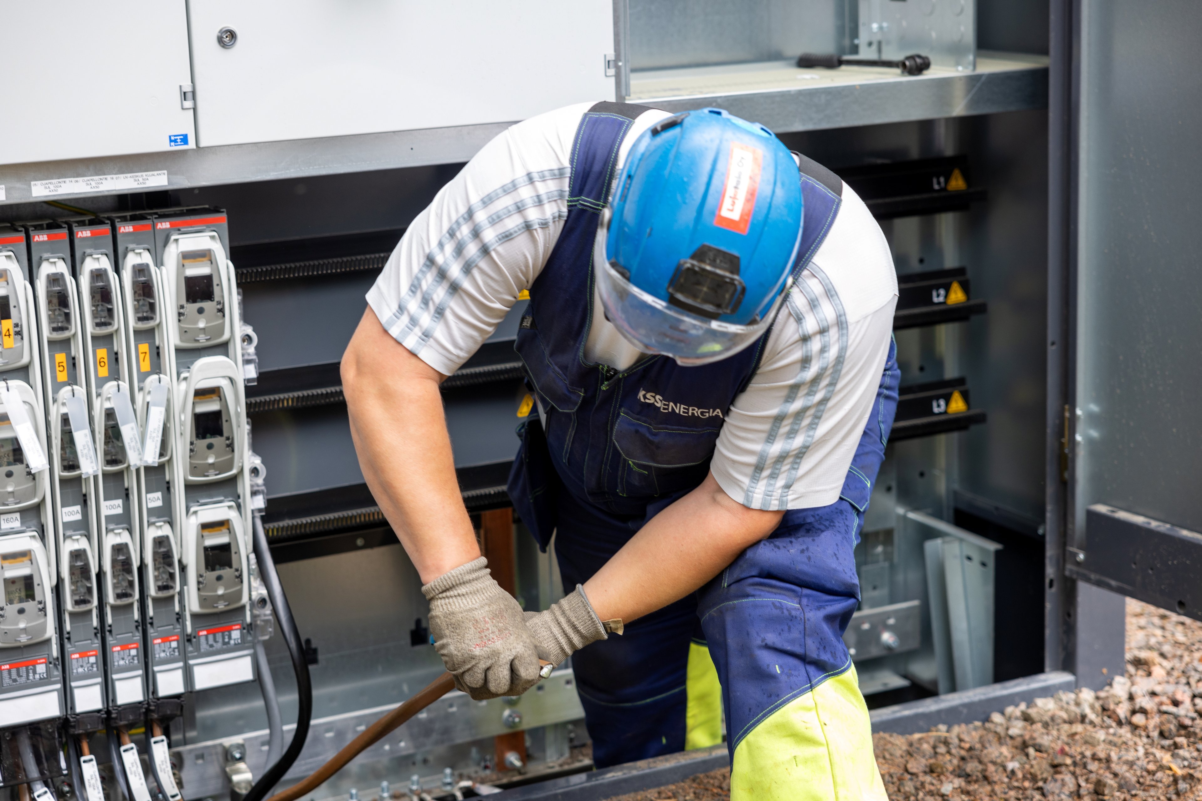 Henkilö suojavarusteissaan kytkee sähkökaapelia muuntamon kytkimeen.