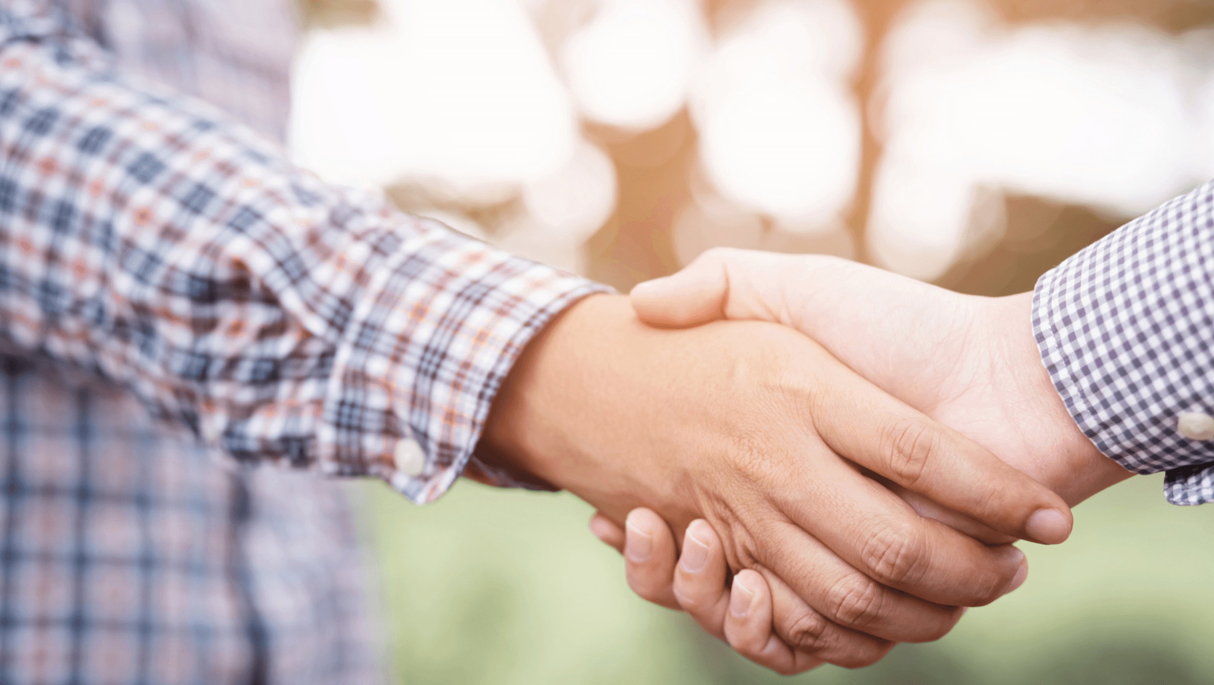 Kaksi ruutupaitaista miestä kättelee pihalla aurinkoisessa säässä.