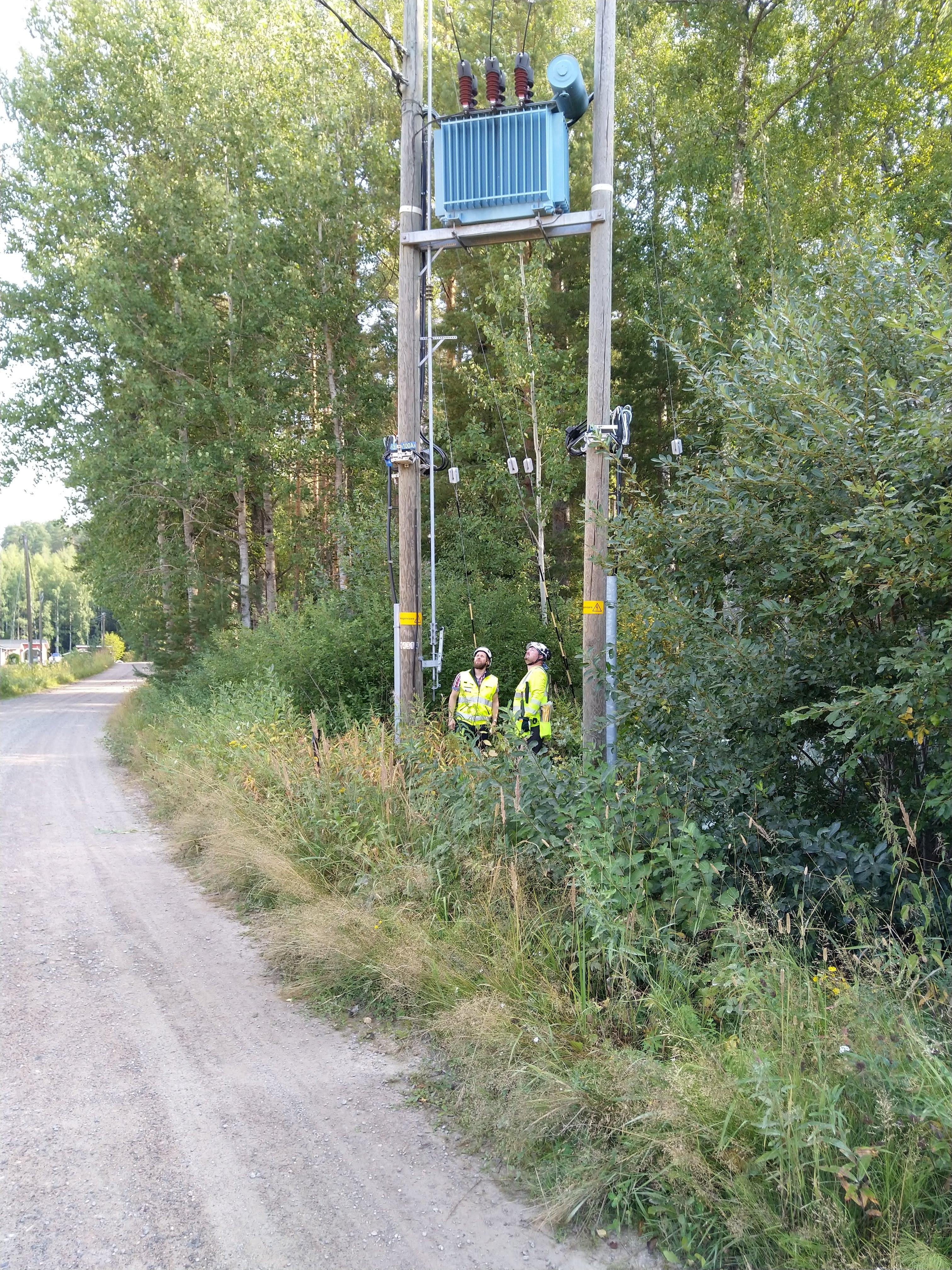 Kaksi henkilöä suojavarusteissa tutkii pylväsmuuntamoa.