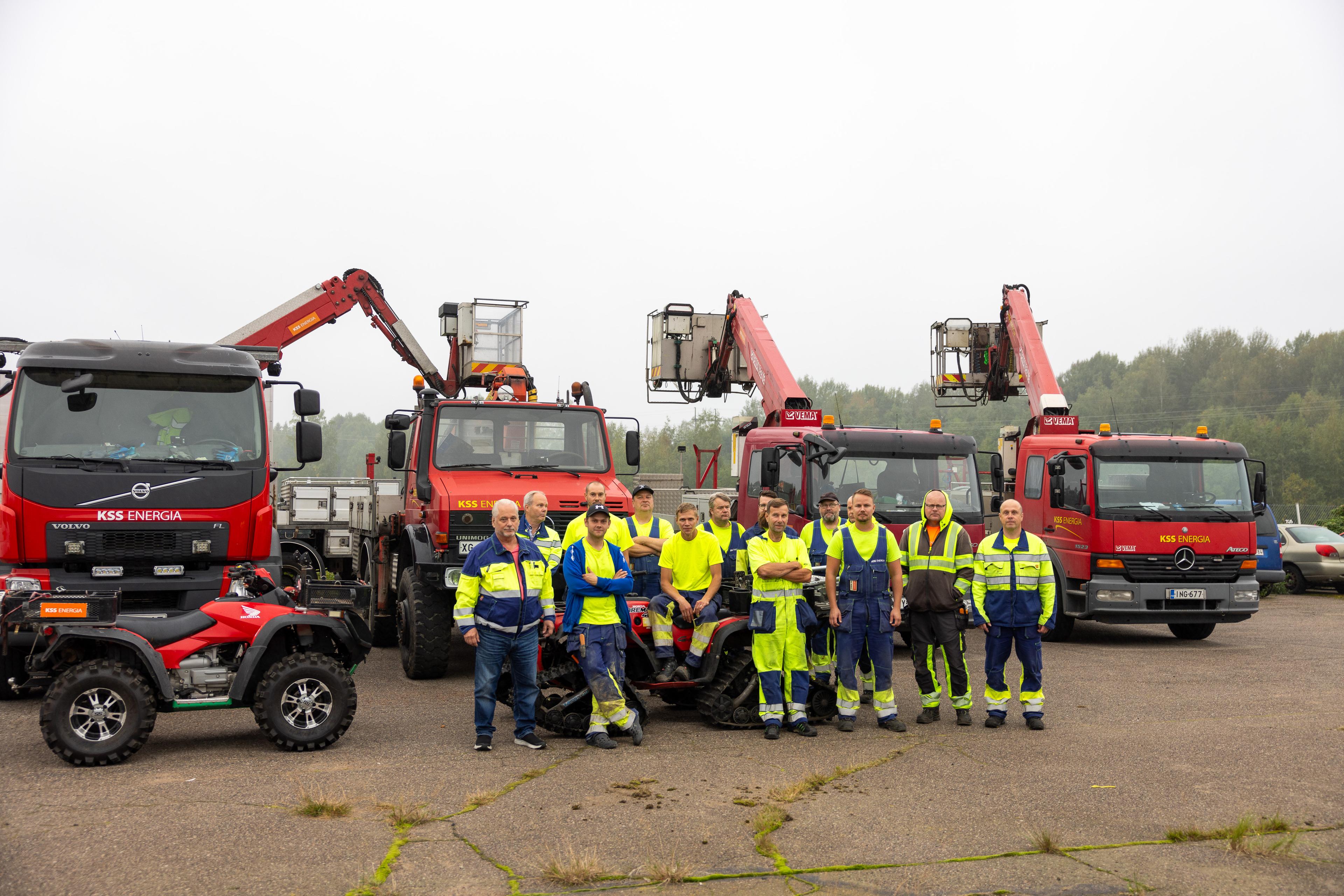 Punaisten nostokoriautojen edessä joukko suojavaatteissa olevia henkilöitä. Kuvan vasemmassa reunassa punainen mönkijä.
