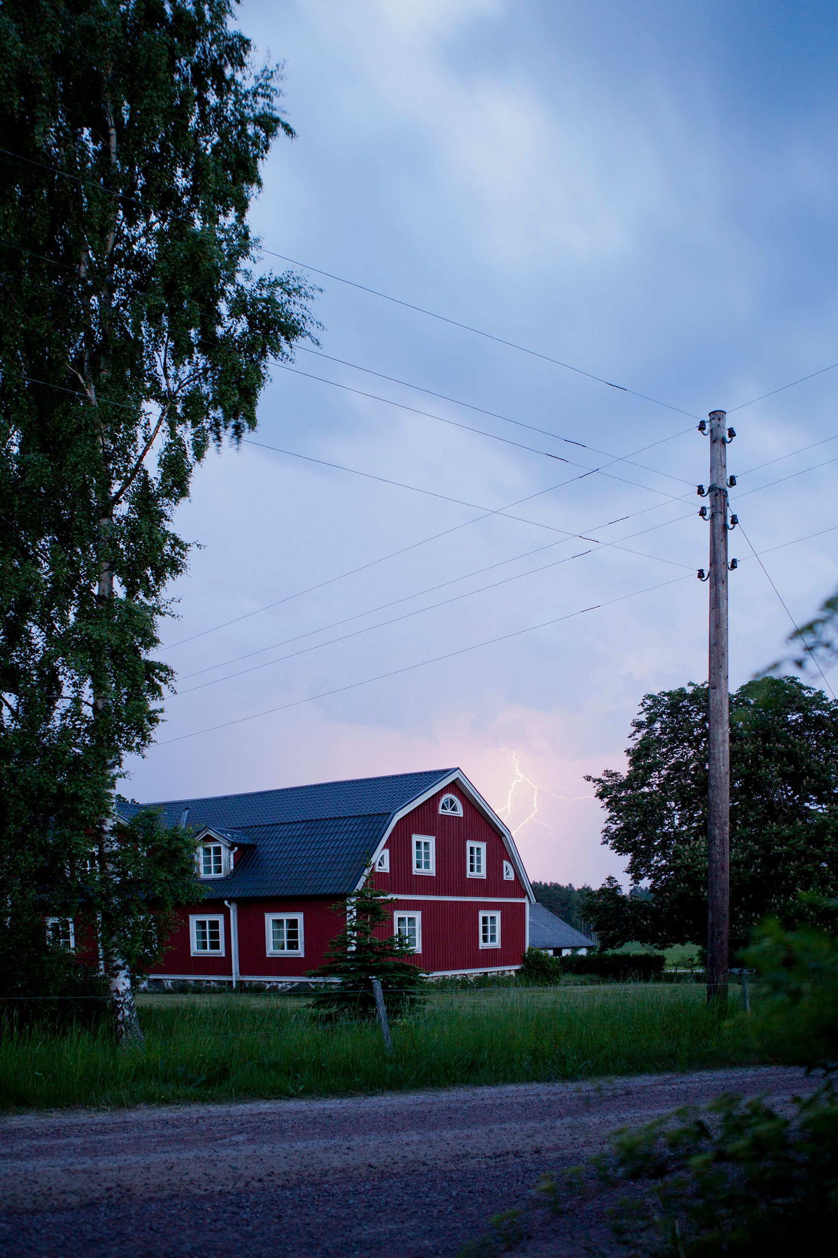 Ilmassa kulkee sähköjohtoja moneen suuntaan punaisen talon lähistöllä, myrskyisellä taivaalla näkyy salamanisku.