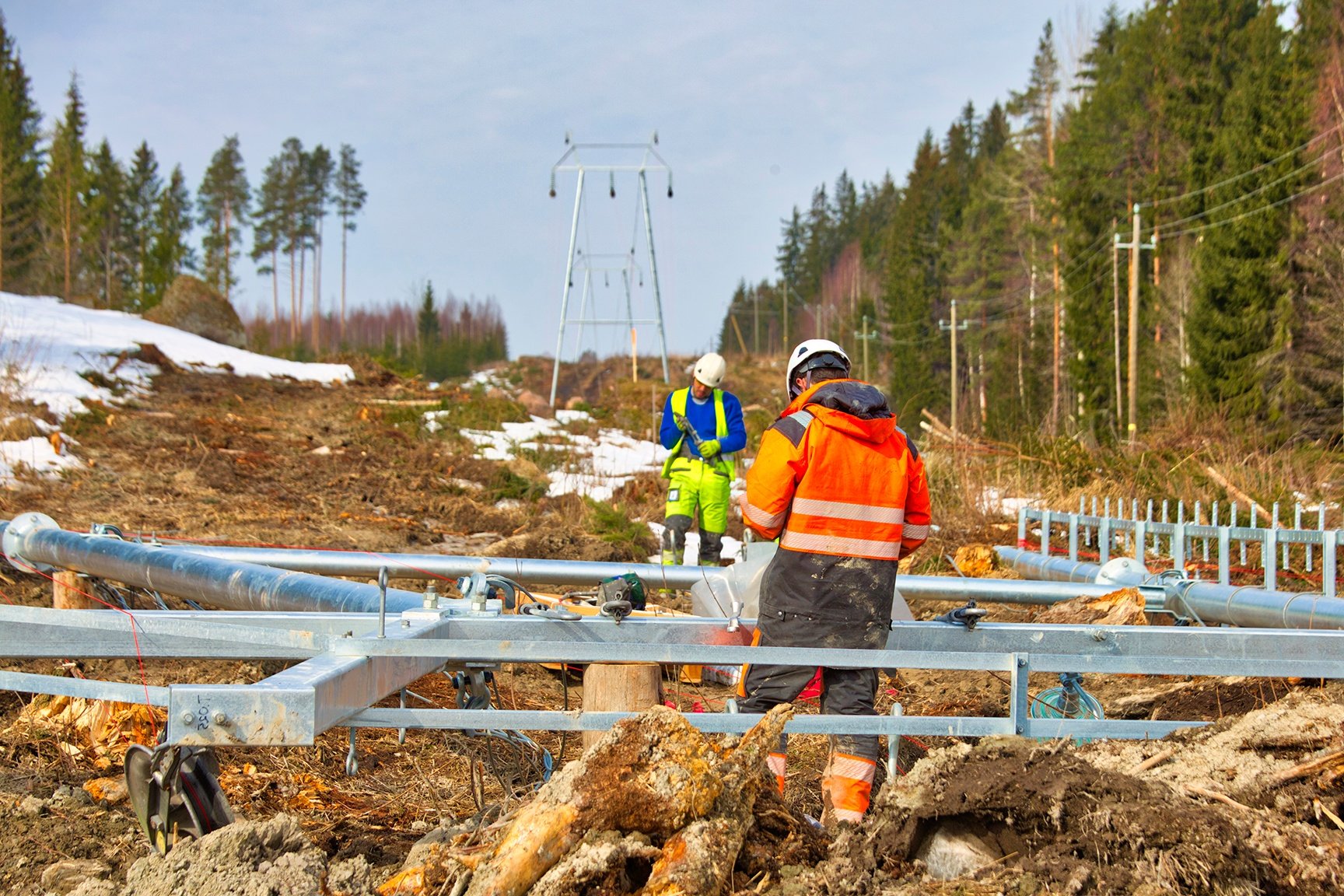 Kaksi työntekijää rakentamassa uutta voimalinjaa. Johtokatu on raivattu ja linjan rakenteita ollaan kokoamassa.