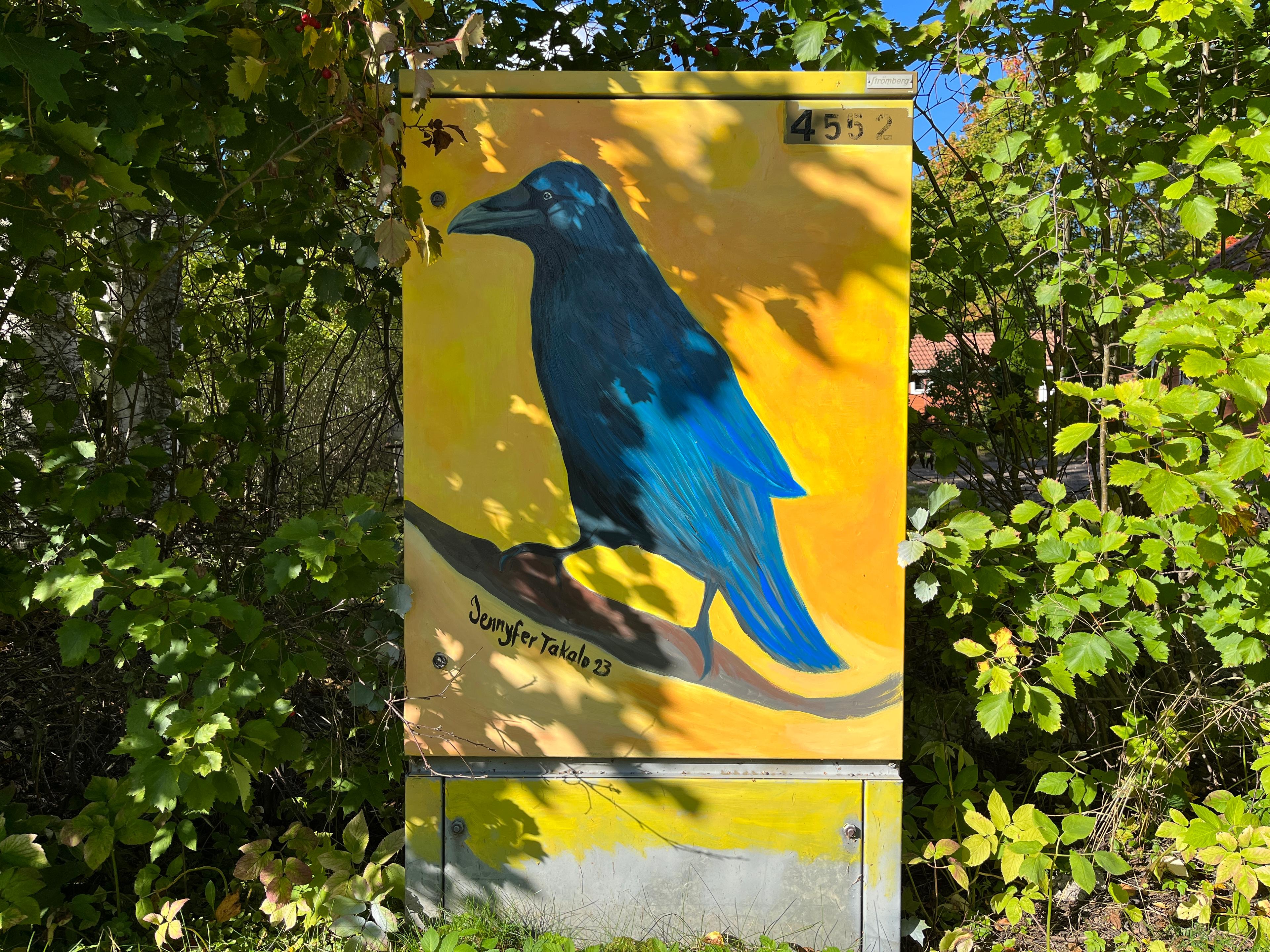 Keltaisella taustalla sininen varis, joka seisoo oksalla.