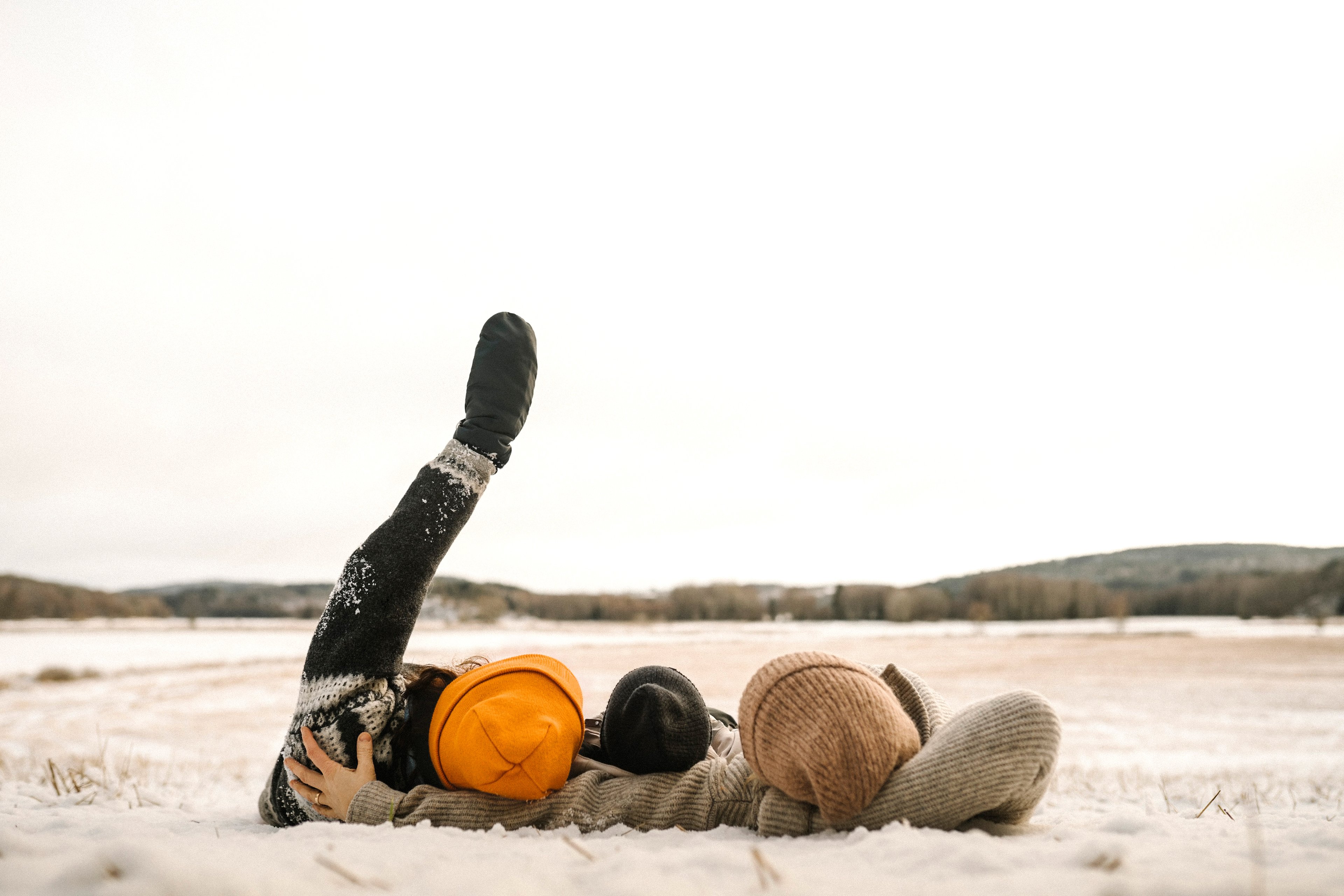 Kuvassa vanhemmat ja lapsi makaavat talvisella pellolla katsellen taivaalle. Toinen aikuisista näyttää kädellä ylös taivaalle vaalealle taivaalle. Toisella vanhemmalla on oranssi pipo ja toisella vaalean ruskea. Lapsella heidän välissä on musta pienempi pipo. Taustalla näkyy lumista peltoa ja kauempana on metsää.
